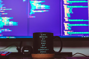 photo of a mug in front of a monitor with code