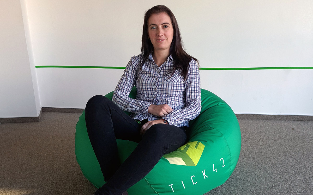 Telerik Academy Alpha graduate in a shirt with square pattern sitting on a green pouf with Tick42 logo on it